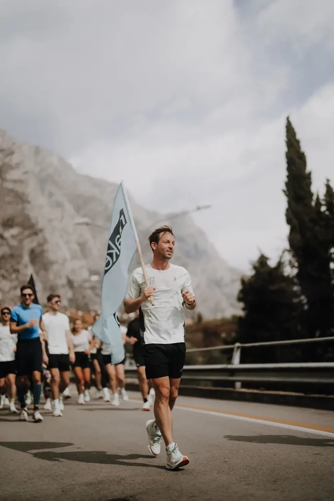Läufer mit großer Flagge und Laufgruppe und Berge im Hintergrund